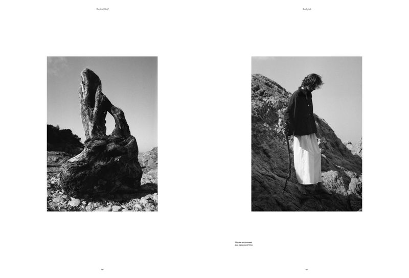 Monochrome editorial-style shot of a rocky outcrop with a natural arch and a lone figure in flowing skirt on a rocky cliff.