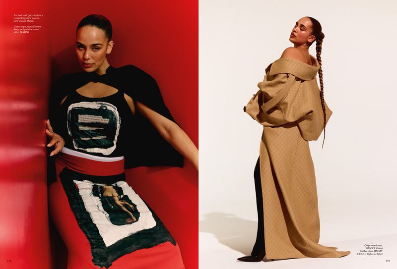 Editorial fashion shot of a woman in an art-inspired black top and skirt, side view in a beige overcoat, red and white background.