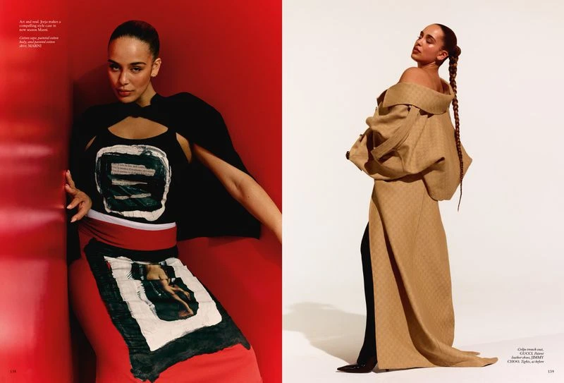 Editorial fashion shot of a woman in an art-inspired black top and skirt, side view in a beige overcoat, red and white background.