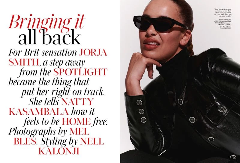 Portrait of singer Jorja Smith wearing black sunglasses and a black leather jacket against a white background in a magazine editorial.