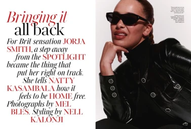 Jorja Smith wearing black sunglasses, a black turtleneck, and a glossy black jacket against a plain white background