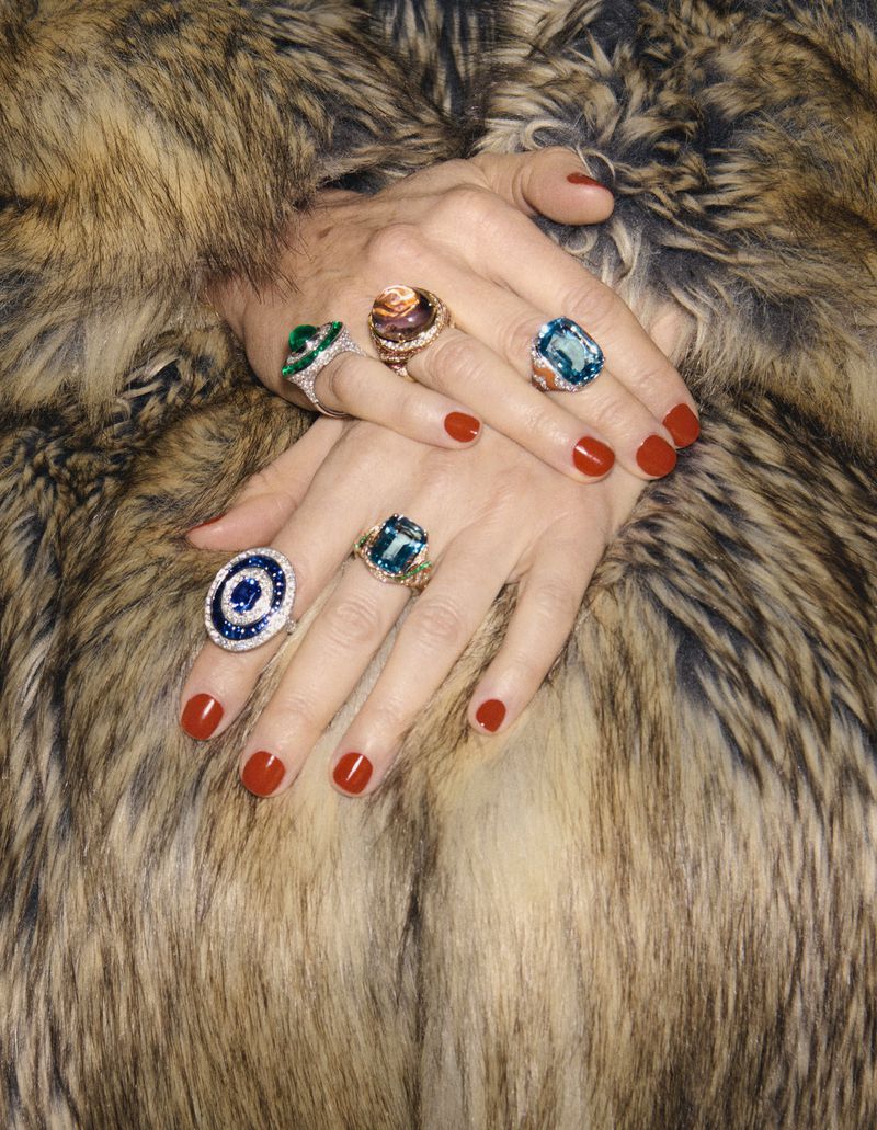 Close-up on a woman's hands adorned with multiple statement rings, set against a luxurious fur coat backdrop, highlighting jewelry.