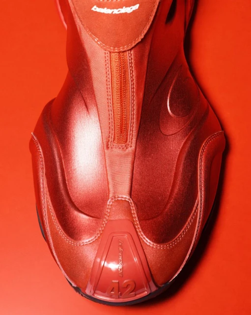 Close-up of a red Balenciaga sneaker on a red background, featuring a zippered front and the brand logo at the top of the shoe.