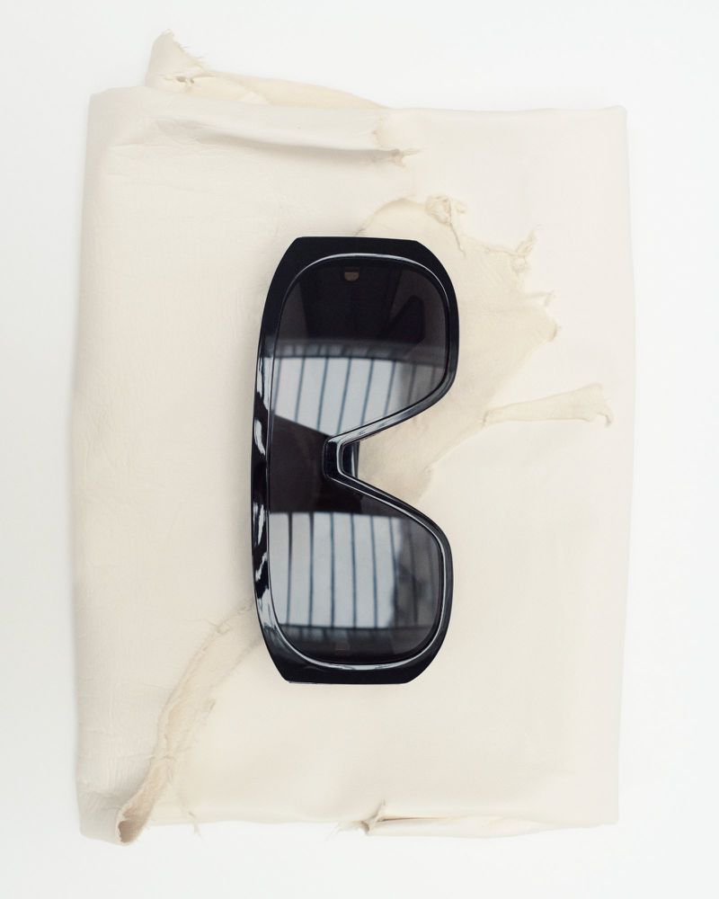 Overhead shot of black sunglasses lying on crumpled off-white paper in a studio setting with natural, diffused lighting.