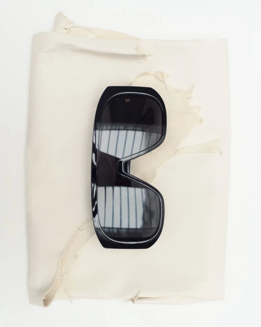 Overhead shot of black sunglasses lying on crumpled off-white paper in a studio setting with natural, diffused lighting.