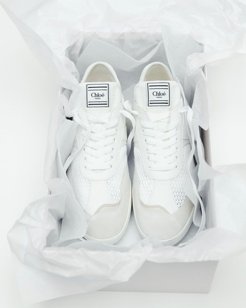 White Chloé sneakers are presented in a box with tissue paper, showcasing their design and brand. Ideal for fashion and product photography.