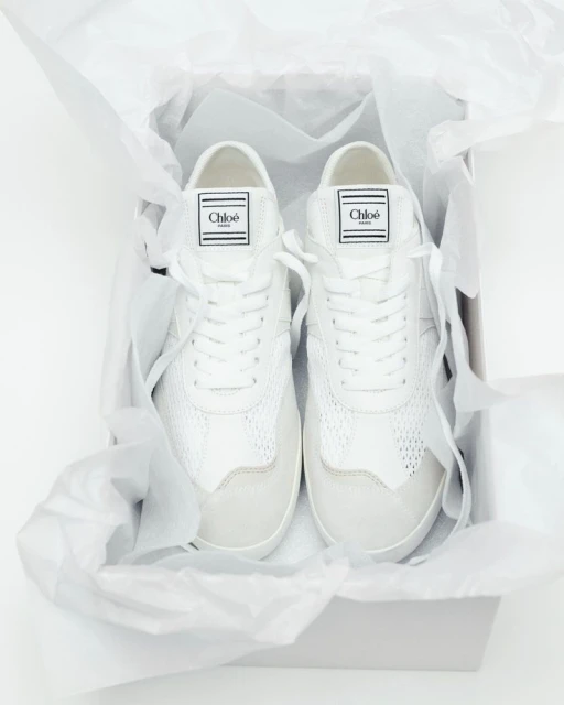 White Chloé sneakers are presented in a box with tissue paper, showcasing their design and brand. Ideal for fashion and product photography.