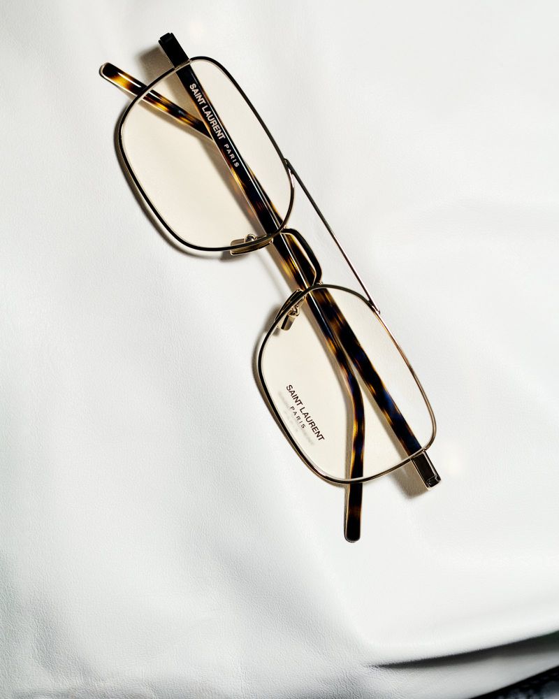 Stylish Saint Laurent eyeglasses with a thin gold frame and tortoiseshell arms are displayed on a smooth white surface.