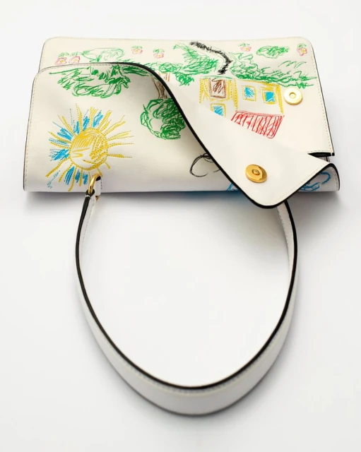 White leather satchel-style handbag features a colorful doodle art design and a handle, presented on a seamless white backdrop.