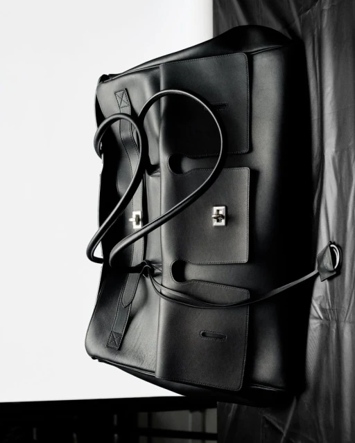 Black leather tote bag with silver hardware, photographed in a studio setting against a white and black draped backdrop.