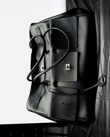Black leather tote bag with silver hardware, photographed in a studio setting against a white and black draped backdrop.