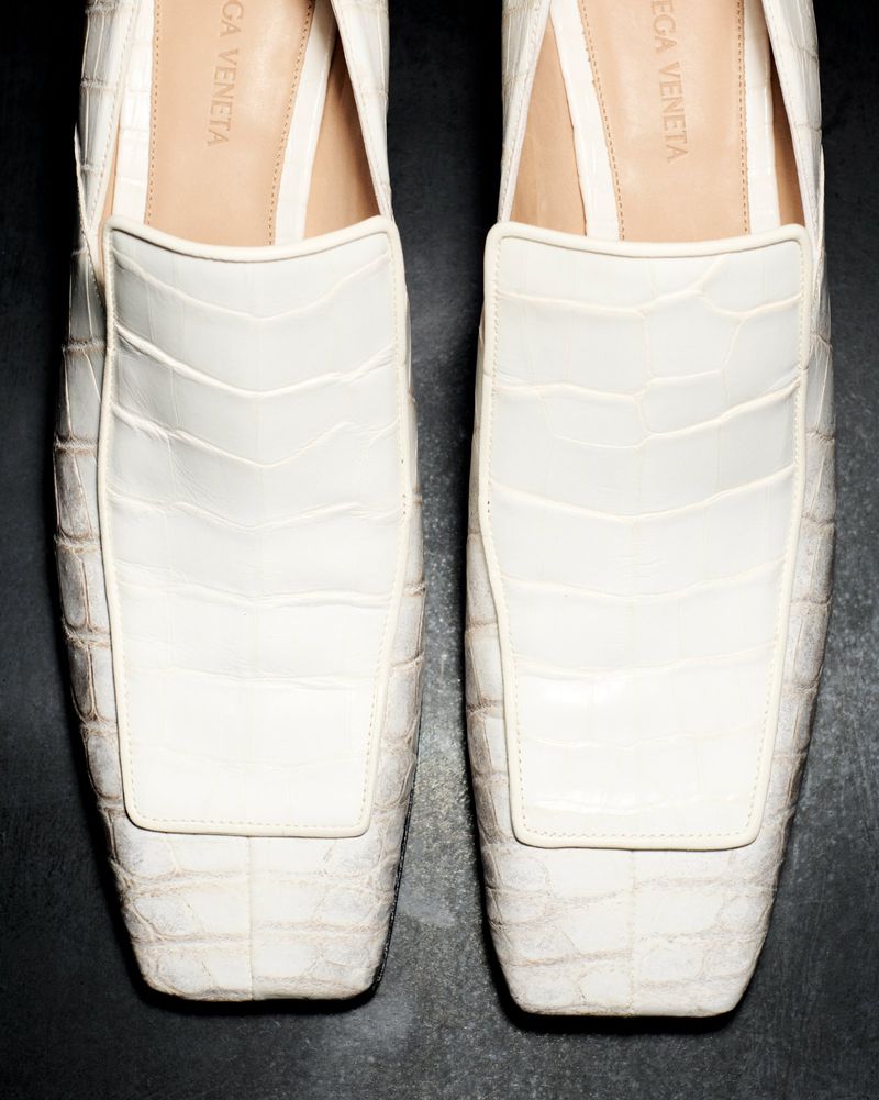 Close-up of white leather slip-on shoes featuring textured alligator pattern, set against a dark backdrop emphasizing fashion footwear.