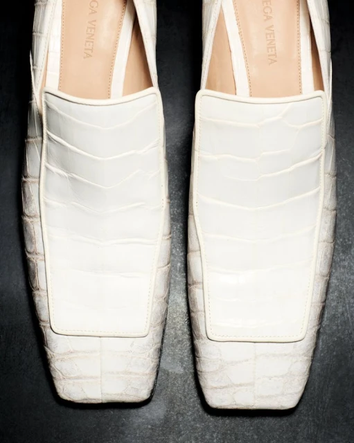 Close-up of white leather slip-on shoes featuring textured alligator pattern, set against a dark backdrop emphasizing fashion footwear.