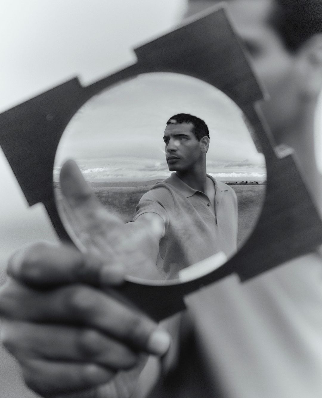 Monochrome portrait of a man looking through a lens with a field and sky background, captured with creative photography techniques.