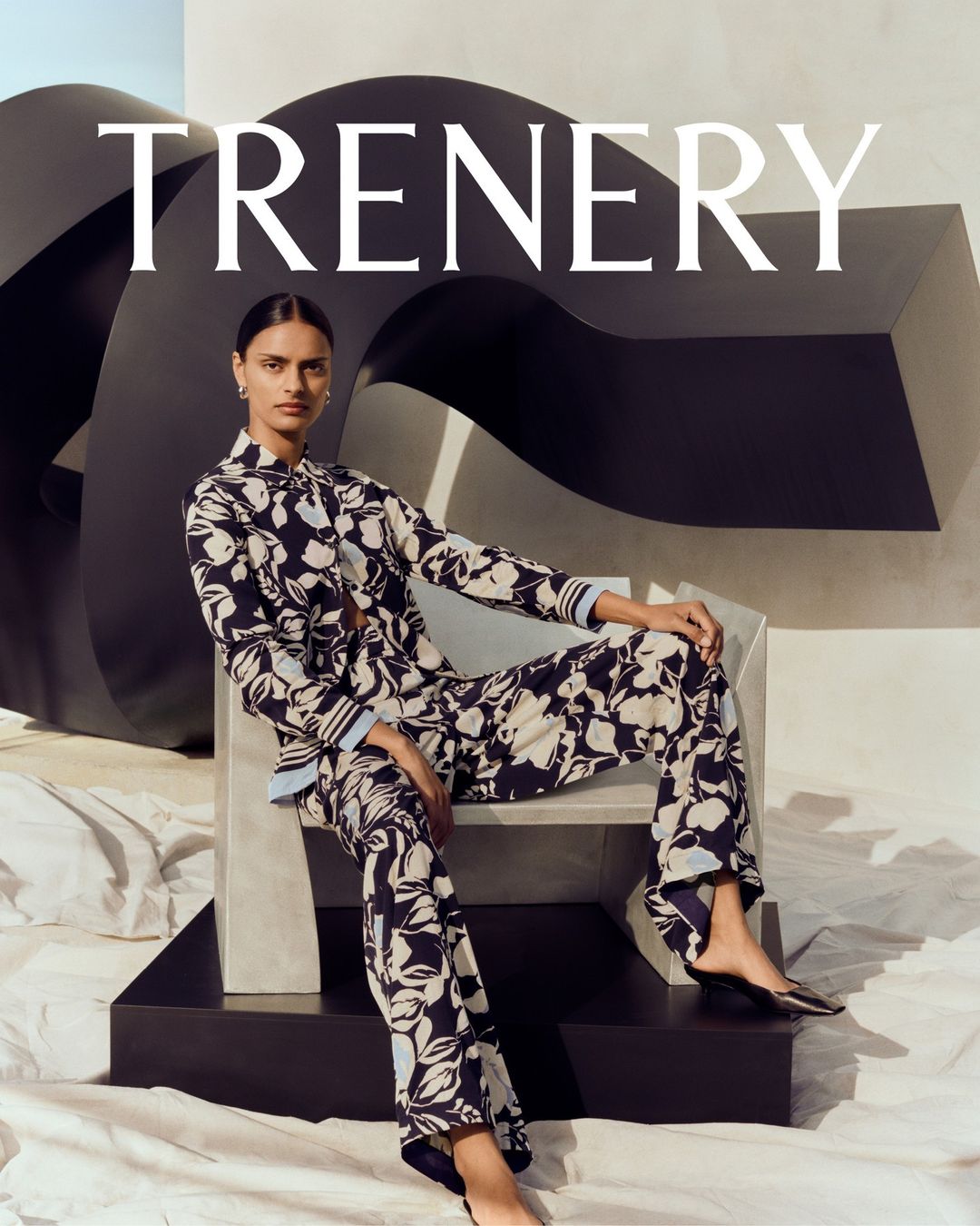 Woman in floral pajamas poses in a fashion shot in front of a black sculptural form with crumpled fabric on the ground.