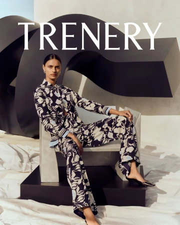 Woman in floral pajamas poses in a fashion shot in front of a black sculptural form with crumpled fabric on the ground.