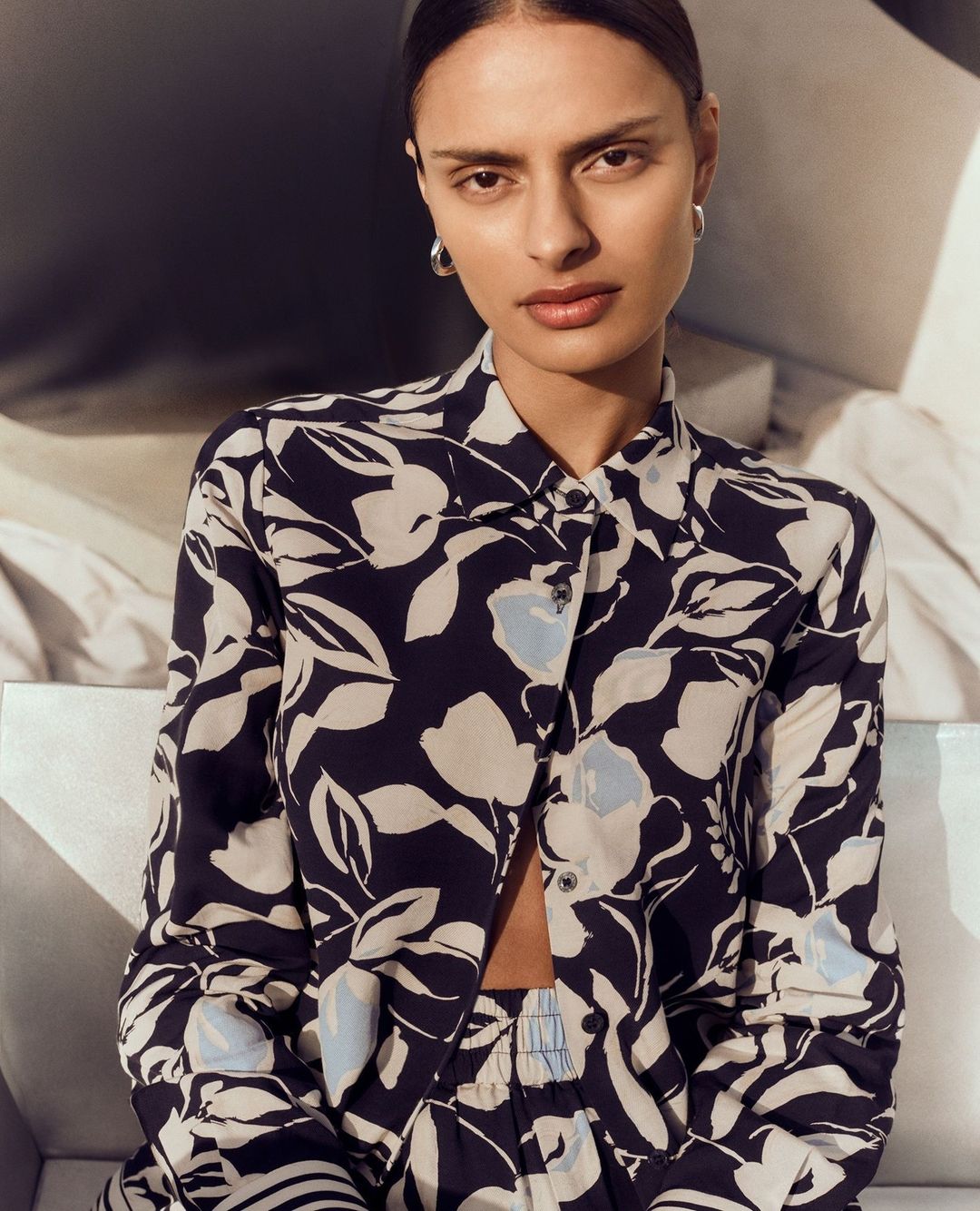 Model wearing a blue and white floral print silk shirt and matching trousers in a soft lit indoor setting
