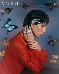 Model Taleedah Tamer in an orange blouse wearing a large bee ring and insect hairpiece surrounded by butterflies for Mojeh Magazine.
