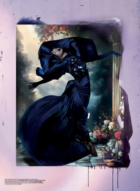 A woman in a blue gown strikes a pose within a framed artwork featuring a classical column and painted floral accents, under studio lighting.