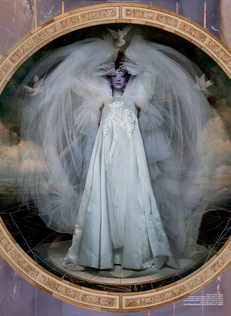 Elegant fashion shot of a woman in an ornate white dress and veil, styled with dove accents, set against a marble and cloud background.