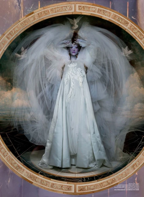 Elegant fashion shot of a woman in an ornate white dress and veil, styled with dove accents, set against a marble and cloud background.