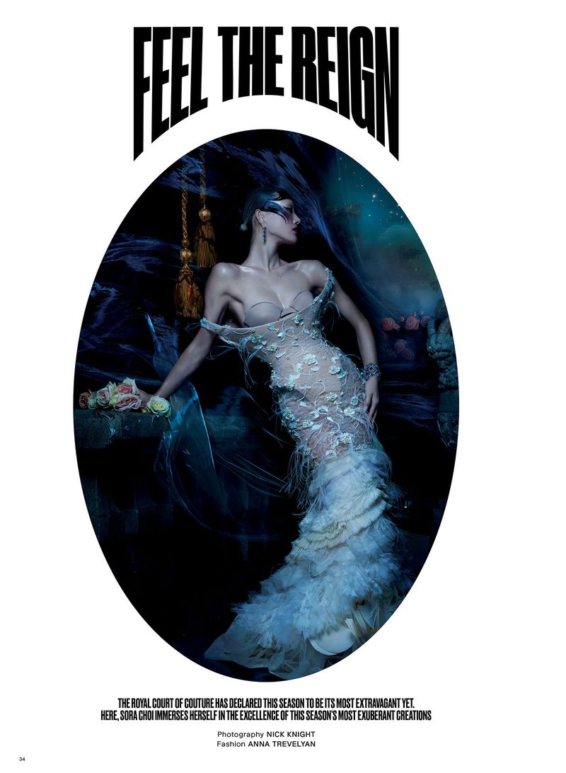 Fashion editorial image featuring a woman in a sheer white feathered gown with a mask, posing in a dramatically lit, ethereal setting.