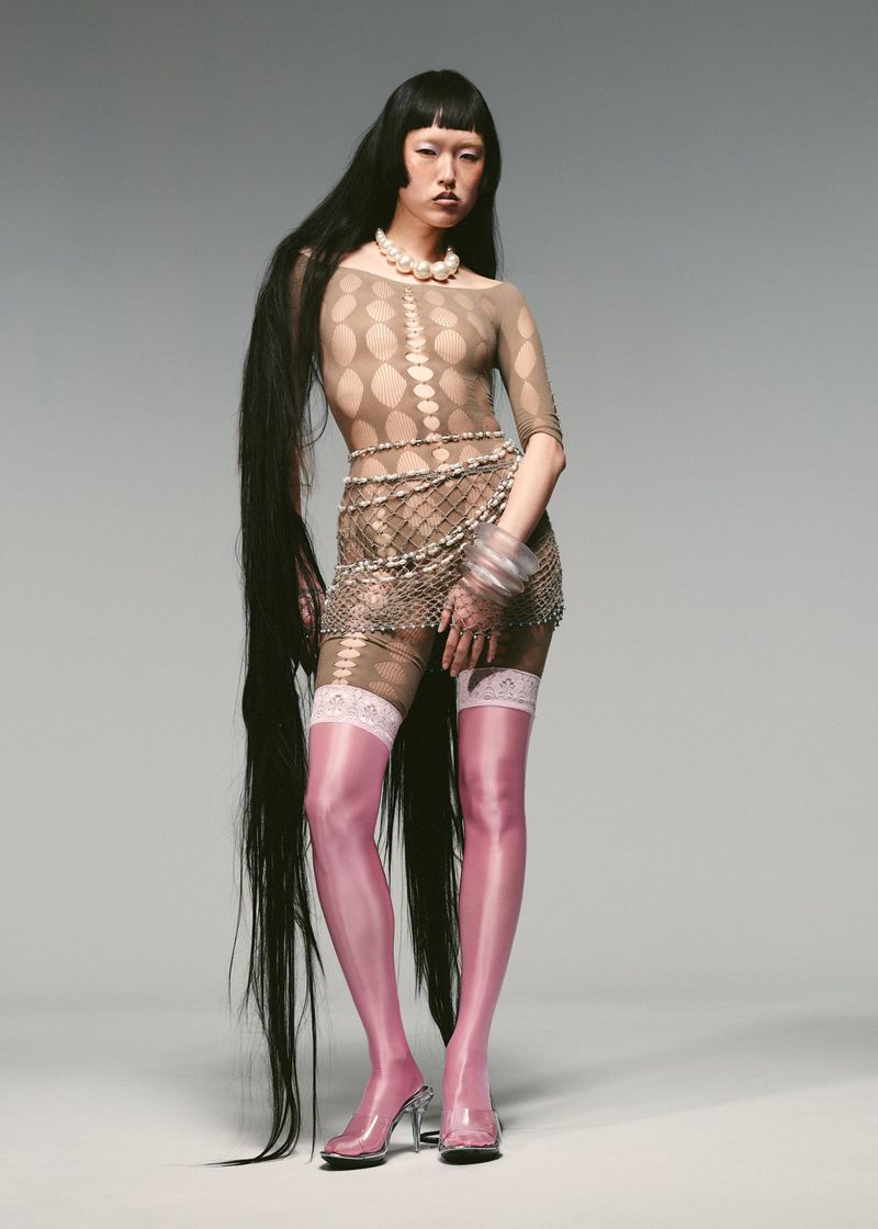 A full-length studio shot of a slender Asian woman with very long, dark hair, pink thigh-high stockings, and clear heels.