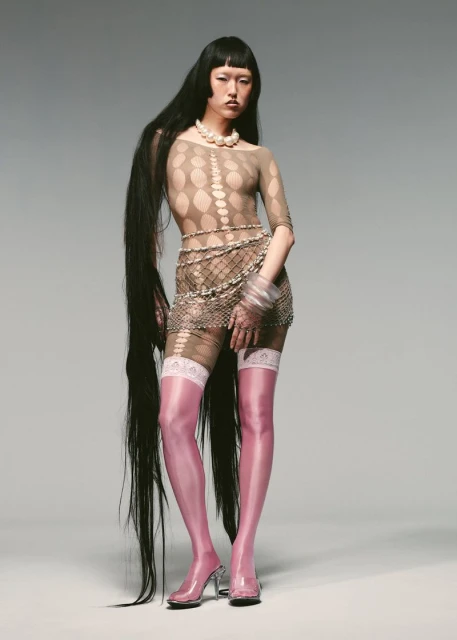 A full-length studio shot of a slender Asian woman with very long, dark hair, pink thigh-high stockings, and clear heels.