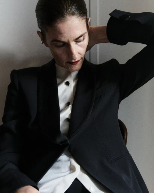 Stylish portrait of an adult female in a dark suit with white button-up shirt. She is posing indoors with a neutral facial expression.