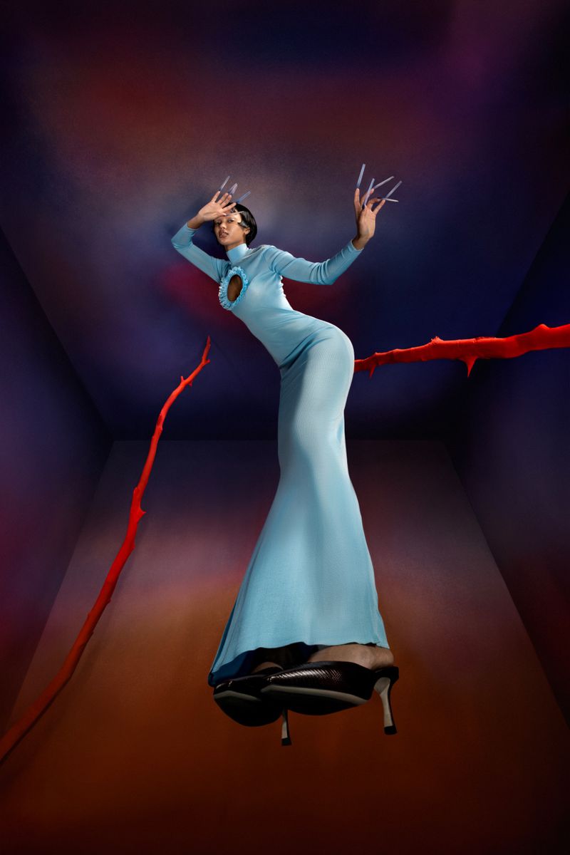 A woman with dramatic makeup and a light-blue dress poses in a room with a surreal and slightly ominous atmosphere, with high heels.