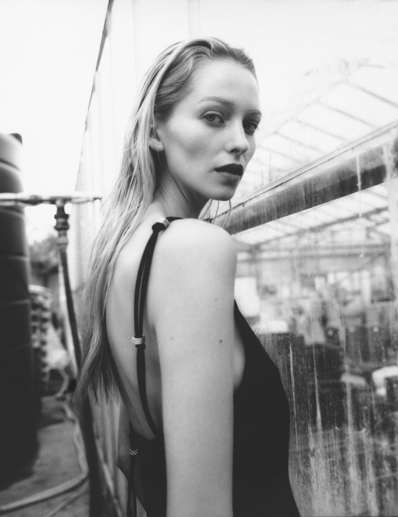 Black and white portrait of a fair-skinned woman with wet, blonde hair in a black low-backed dress looking over her shoulder.
