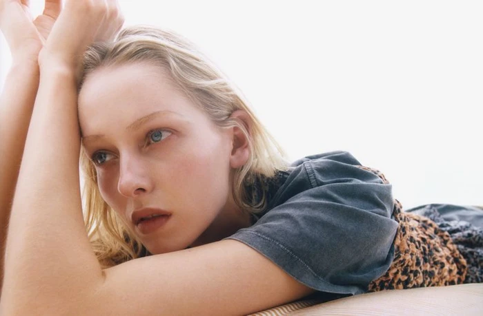 Model with blonde hair resting arms above head against a bright white background for Re-Edition Magazine