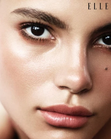 Close-up portrait of a fair-skinned adult female face showcasing soft makeup, highlighting eyes and lips, and featuring the 'Elle' logo.