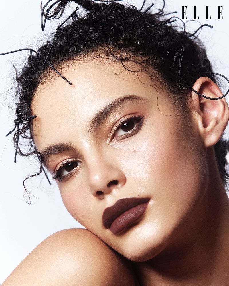 Close-up portrait of a woman with dark, curly hair and deep red lipstick. Head and shoulders, neutral background, beauty and fashion style.