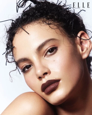 Close-up portrait of a woman with dark, curly hair and deep red lipstick. Head and shoulders, neutral background, beauty and fashion style.