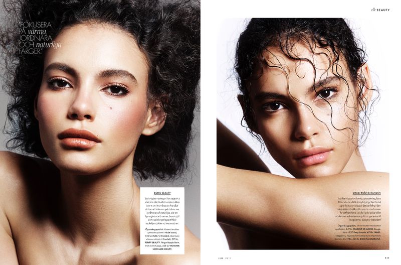 Beauty editorial shot featuring a model with dark, curly hair and neutral makeup posing in a close-up studio portrait.