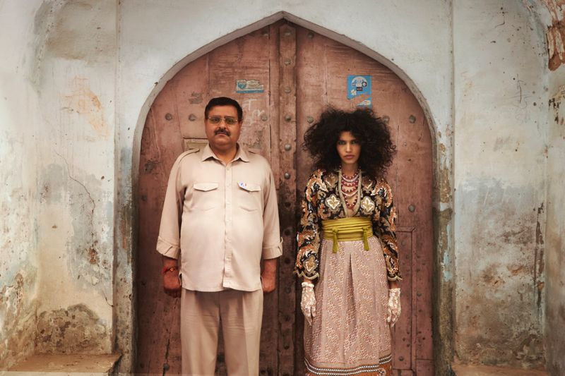 Two people, an adult male and an adult female, standing in front of a weathered, arched doorway with peeling paint and visible brickwork.