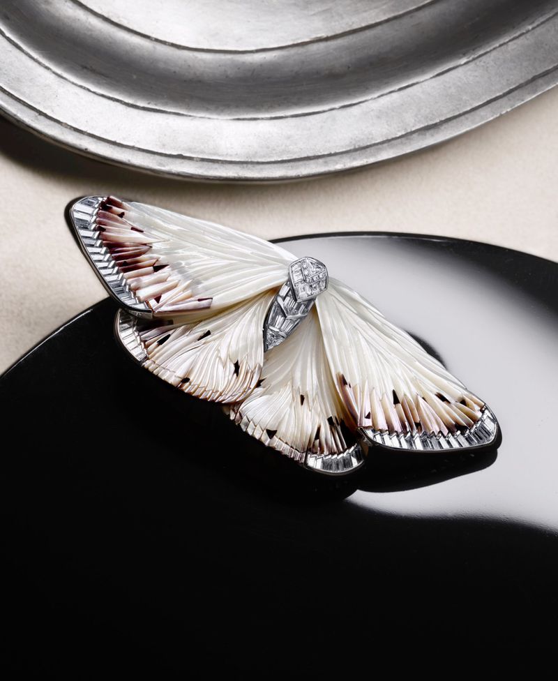 Close-up studio shot of a moth-shaped brooch featuring white and brown wings with a diamond center on a black reflective surface.