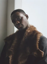 Close-up portrait of a Black man wearing a brown fur collar against a white background for AnOther Man Magazine.
