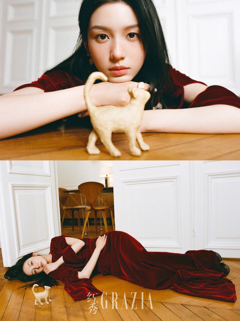 Portrait of an Asian woman in a long-sleeve dress lying on a wooden floor with a ceramic cat, styled for a magazine cover.