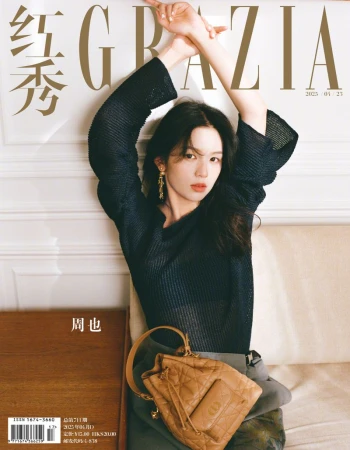 Magazine cover shot of an adult female model with dark hair posing with her arms raised above her head and holding a tan purse.