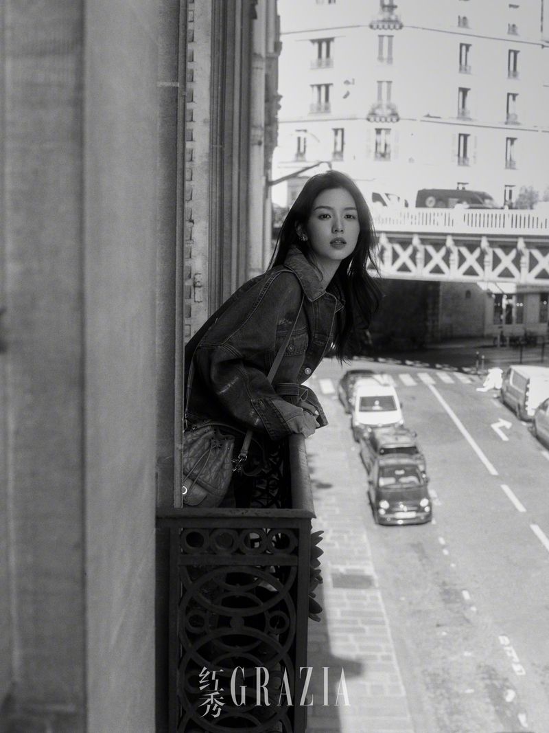 Woman leaning on a balcony railing overlooking a city street in a black and white editorial photograph for Grazia China