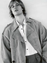 Monochrome portrait of Nicholas Galitzine wearing an open trench coat and white button-down shirt against a plain background