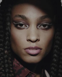 Close-up portrait of a woman with braided dark hair wearing winged eye makeup and patterned collared shirt