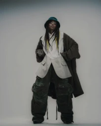 Model wearing dark green bucket hat and layered oversized clothing against a neutral gradient background.