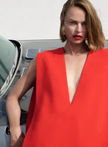 Birgit Kos in a vibrant red V-neck dress leaning against a metallic grey car for Wallpaper Magazine Red Heat editorial.
