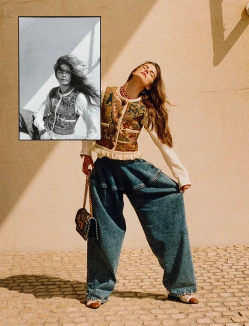 A fashionable young woman poses in an outdoor fashion shot, wearing a tapestry vest, baggy jeans, and jewelry, with a vintage photo.
