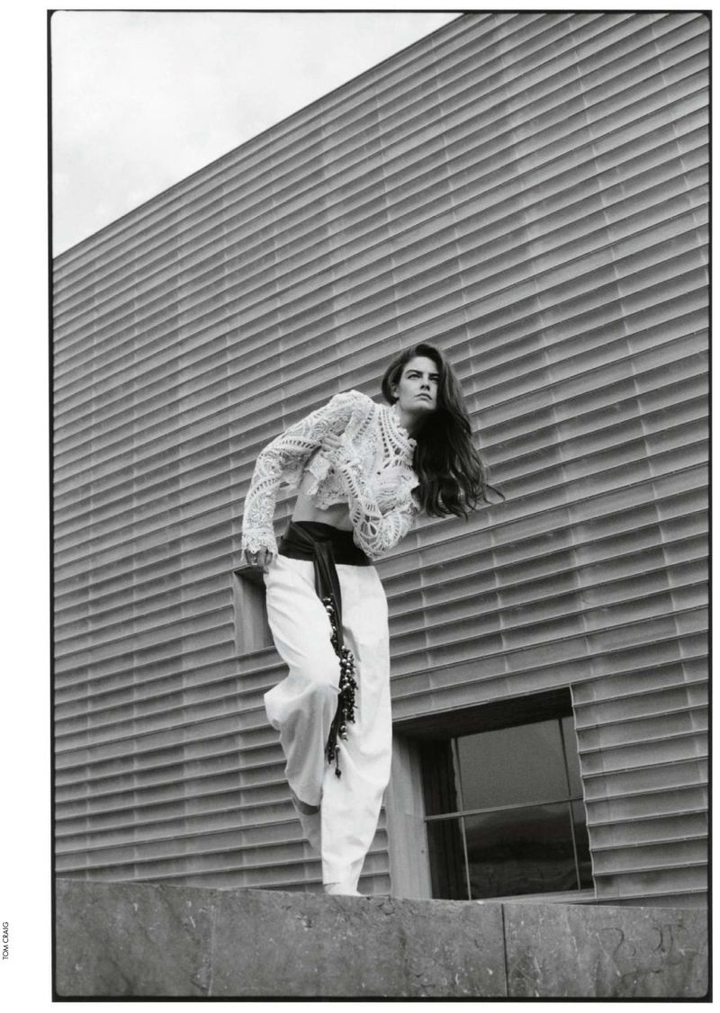 Fashion shot in black and white features a woman in white lace top and pants posing against a modern, horizontally ribbed building.