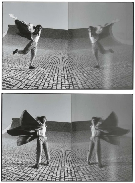 Monochrome studio shot: woman poses outdoors with large flowing cape, reflected multiple times in the background, creating a surreal effect.