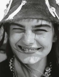 Close-up portrait of model Merlijne Schorren wearing a decorated hat, captured in black and white by Tom Craig.